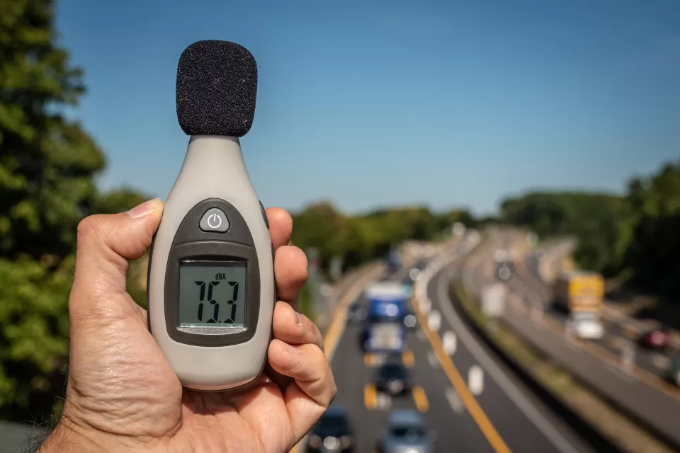 Close-up of hand holding up decibel meter with blurred highway with traffic in background